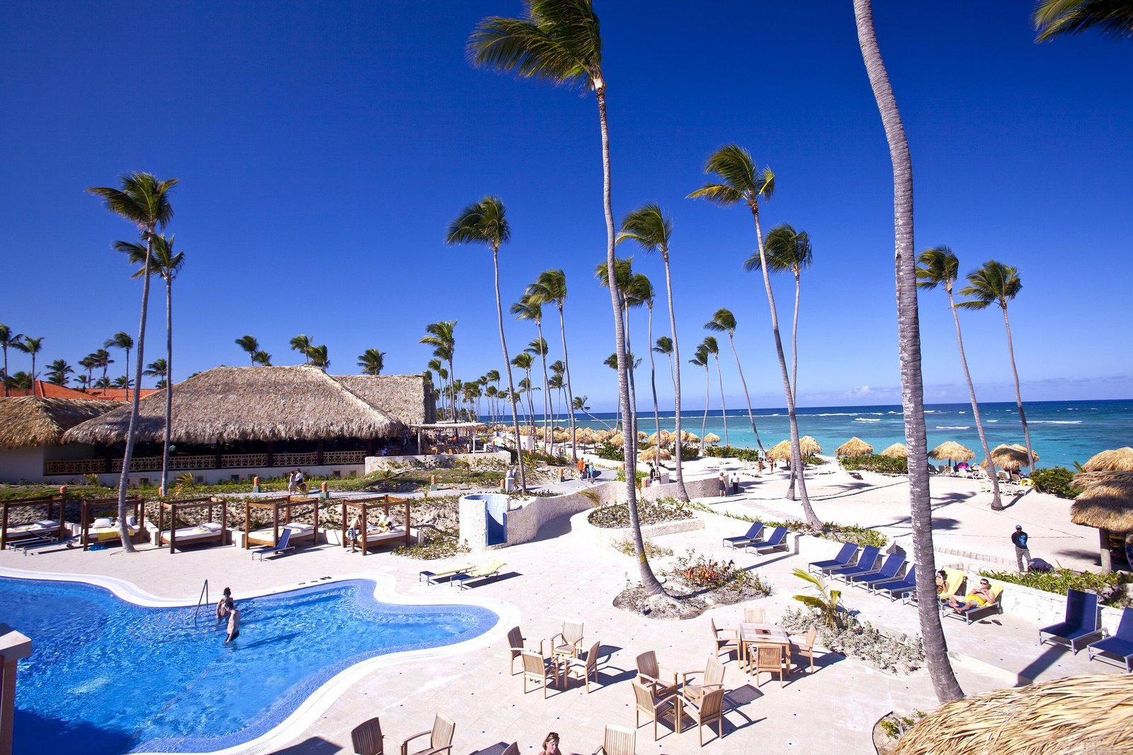 Piscina, palmeras y playa de un resort en Punta Cana